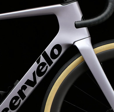 Entdecke jetzt das Orbea Orca! Ein dunkelblaues Rennrad steht auf feinem Schotter vor einer Bergkulisse.