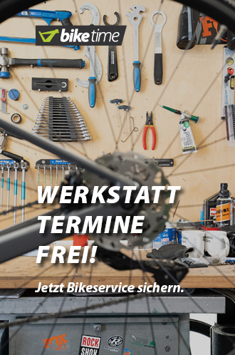 Werkstatt-Termine frei: Jetzt Bikeservice sichern. Im Vordergrund des Bildes ist das hintere Rad eines Fahrrads erkennbar, allerdings nicht im Fokus. Im Hintergrund ist die Werkzeugwand einer Fahrrad-Werkstatt erkennbar.