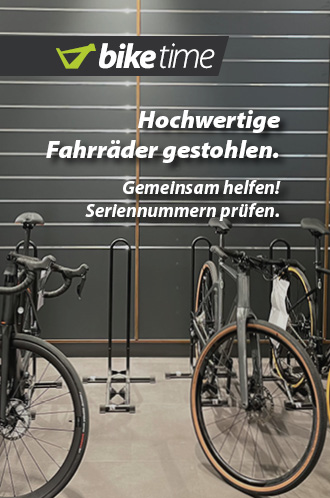 Hochwertige Fahrräder gestohlen. Gemeinsam helfen! Seriennummern prüfen. Zu erkennen sind zwei Rennräder in Bikeständern in einer Verkaufshalle. Zentral in der Mitte ist ein leerer Bikeständer zu sehen.