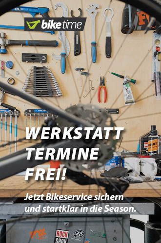 Werkstatt-Termine frei: Jetzt Bikeservice sichern und startklar in die Season. Im Vordergrund des Bildes ist das hintere Rad eines Fahrrads erkennbar, allerdings nicht im Fokus. Im Hintergrund ist die Werkzeugwand einer Fahrrad-Werkstatt erkennbar.