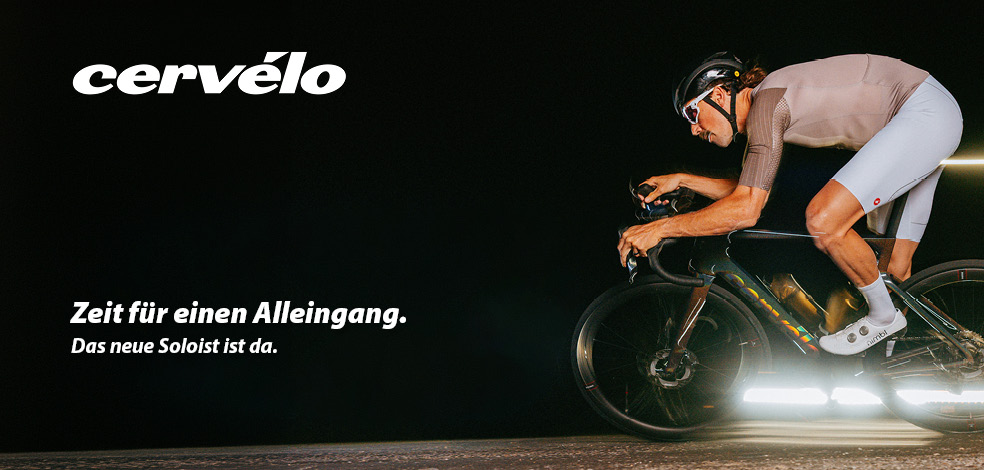 Ein Fahrradfahrer fährt auf einem Rennrad vor sehr dunklem Hintergrund.