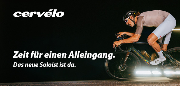 Ein Fahrradfahrer fährt auf einem Rennrad vor sehr dunklem Hintergrund.