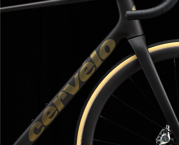 Das neue Cervelo R5: Gnadenlos leicht. Entwickelt für die steilsten Anstiege. Zu sehen ist ein Ausschnitt eines schwarzen Fahrradrahmens. Zu sehen sind Teile des Oberrohrs, des Unterrohrs, des Reifens, des Lenkers und der Gabel. Die Wortmarke „Cervelo” ist lesbar.
