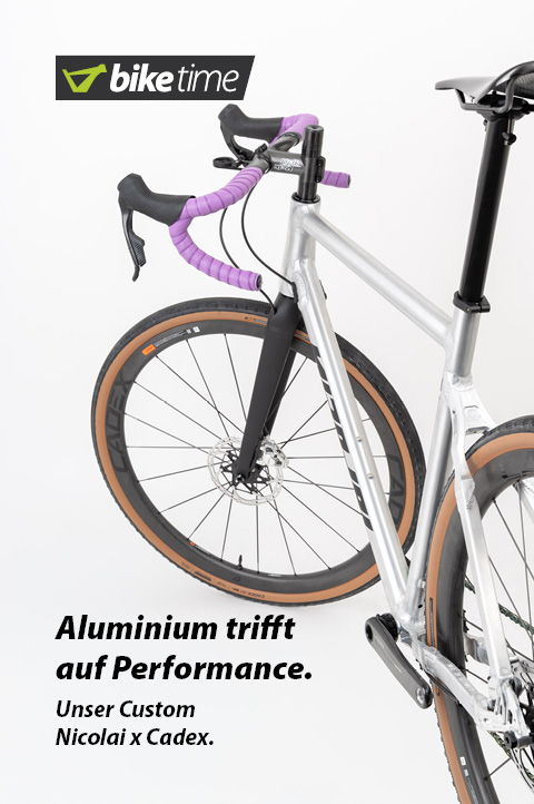 Zu erkennen ist ein Gravel-Bike von hinten mit nach links eingeschlagenem Lenker. Silberner Rahmen, schwarze Laufräder und ein violettes Lenkerband.