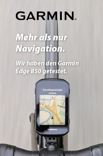 Zu erkennen ist ein Radcomputer, der auf einem Lenker eines Rennrads montiert ist. Das Bild zeigt den Radcomputer von oben, sodass auch die befahrene Straße sichtbar ist. Auf dem Radcomputer ist eine Kartennavigation sichtbar.