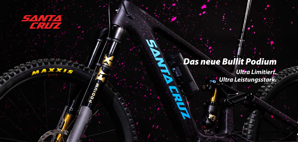 Das neue Bullit Podium: Ultra Limitiert. Ultra Leistungsstark. Zu erkennen ist der Ausschnitt eines schwarzen Fahrrads mit pinken Spritzern. Besonders prägnant ist die Gabel zu sehen - eine Podium-Gabel der Marke Fox. Es handelt sich um ein E-Mountainbike der Marke Santa Cruz - es ist das Bullit Podium.