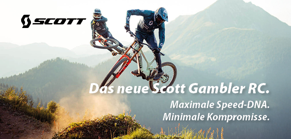 Zu erkennen sind zwei Mountainbiker in hügeligem Gelände die mit ihren Rädern gerade mitten im Sprung sind. Es handelt sich um Mountainbikes der Marke Scott. Das Modell ist das Gambler RC.