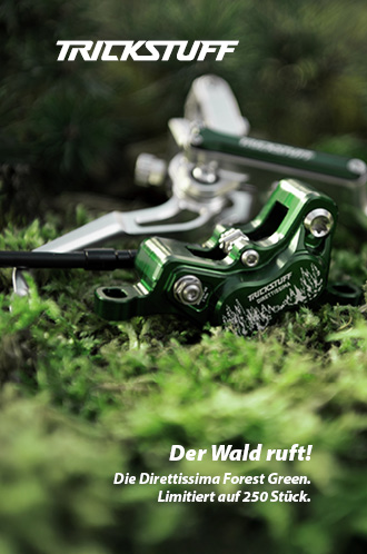 Ein grüner Bremssattel liegt im Moos. Der Bremssattel sieht sehr hochwertig aus und hat eine aufwendige Gravur, die einen Wald und die Wortmarke Trickstuff Direttissima zeigt.