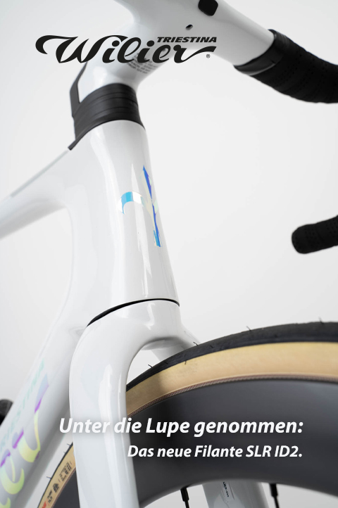 Das Steuerrohr und Teile des Lenkers und Vorderrades eines Fahrrades sind aus der Froschperspektive zu sehen. Rahmen und Lenker sind weiß lackiert. Logo und Wortmarke sind irisierend blaugrün.