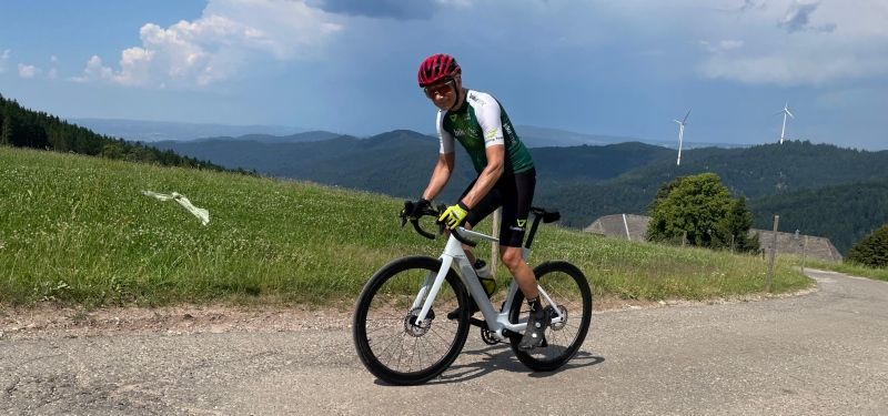 Ein Radfahrer fährt auf einem weißen E-Rennrad eine Rampe hoch und ist links im Bild zu sehen.