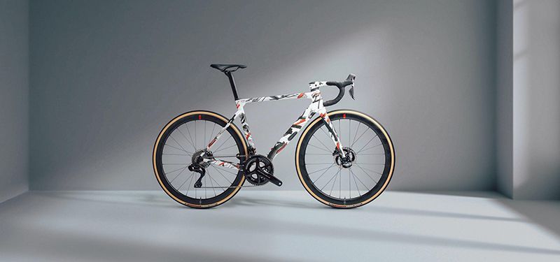 Ein Race-Bike in einem schlichten weißen Raum. Das Fahrrad hat weiß als Basisfarbe und schwarze und rote Streifen randomisiert darüber liegen.