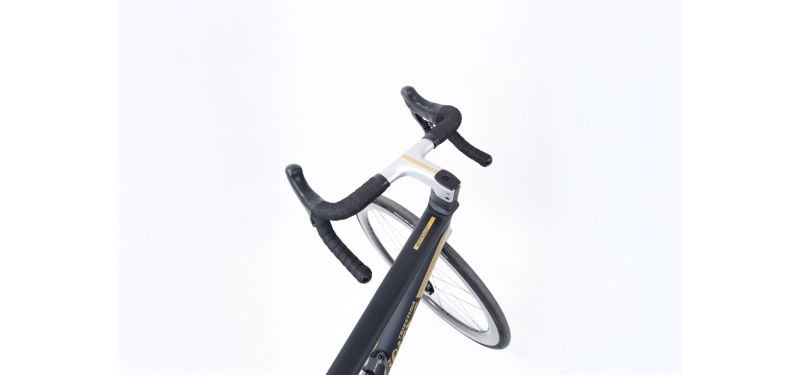 Der vordere Teil eines Rennrads ist erkennbar, als ob die Perspektive des Fahrers eingenommen würde. Es handelt sich um ein schwarz weißes Wilier Veritcale.