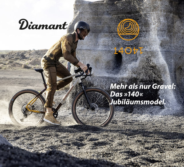 Ein Mann fährt mit einem Gravel Bike über schottriges Terrain. Im Hintergrund ist ein grauer Fels zu sehen.