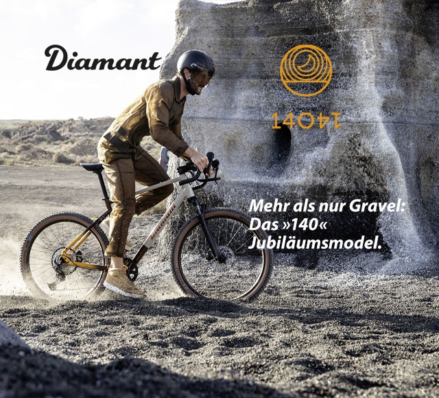 Ein Mann fährt mit einem Gravel Bike über schottriges Terrain. Im Hintergrund ist ein grauer Fels zu sehen.