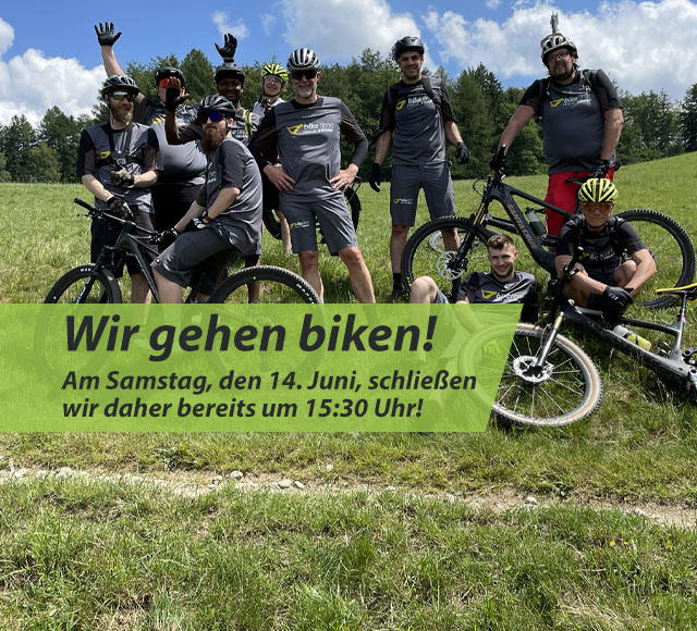 Mehrere Personen stehen auf einer grünen Wiese. Drei Personen sitzen, eine davon auf einem Mountainbike. Ein Mountainbike liegt im Gras, eins wird gehalten. Die Personen tragen Biketime-Trikots.